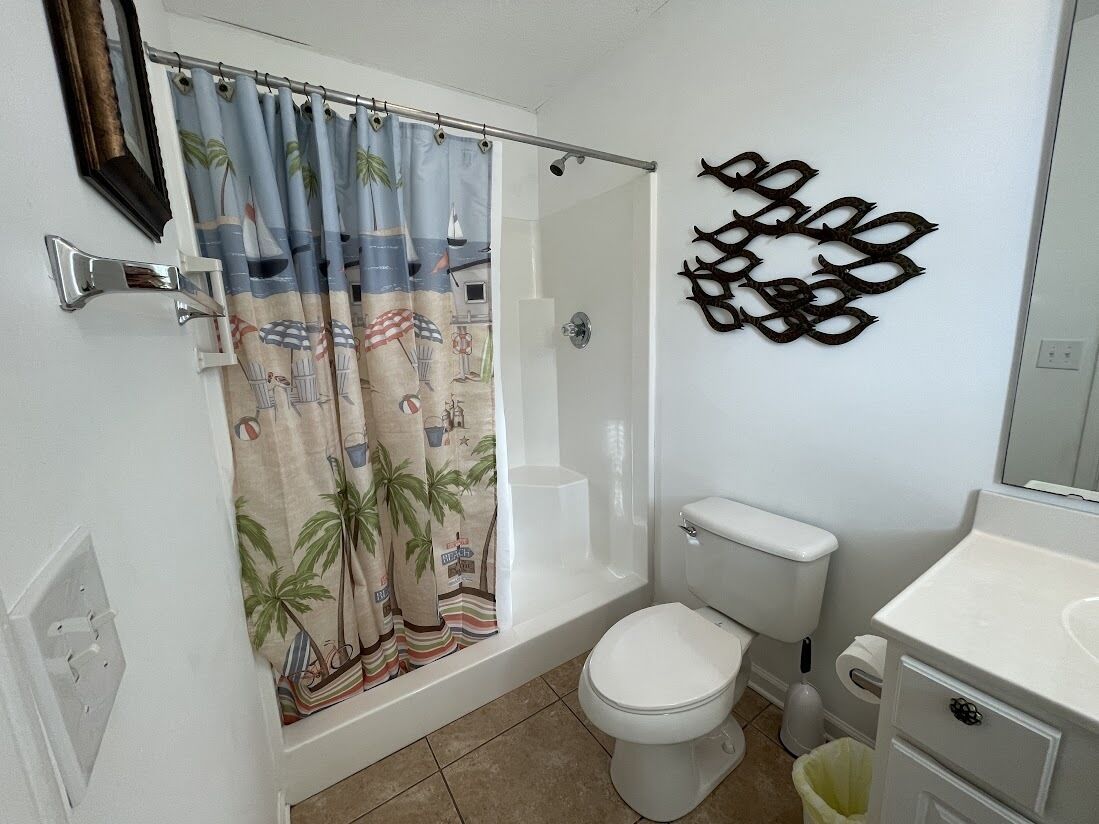 A bathroom with a shower curtain featuring a beach scene, a toilet, a sink, and a wall-mounted decorative piece.