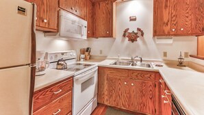 A compact kitchen with wooden cabinets, a white refrigerator, a microwave, a stove, and a sink. - Cozy and comfortable accommodations in picturesque country setting (Hinckley)