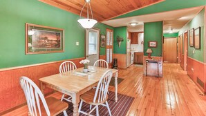 A dining area with a wooden table and white chairs, a hanging light fixture, and a green wall with a framed picture. - Cozy and comfortable accommodations in picturesque country setting (Hinckley)