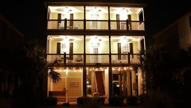 Un edificio de dos pisos con balcones, un porche delantero y una entrada bien iluminada.
