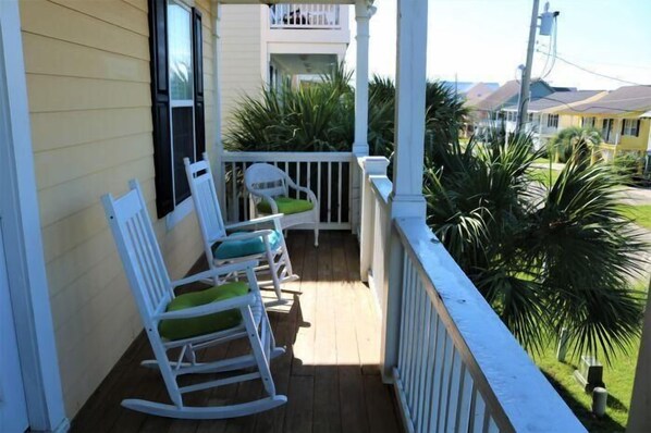 A porch with white rocking chairs and a white railing.