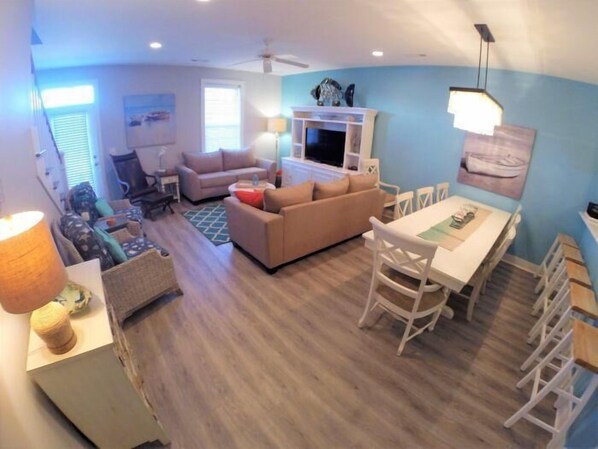 A living room with a sofa, a TV, a dining table with chairs, and a ceiling fan.