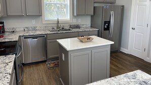 A kitchen with grey cabinets, a stainless steel refrigerator, a dishwasher, and a marble countertop. - Nana's Nook - Second Row in Garden City Beach (Garden City)