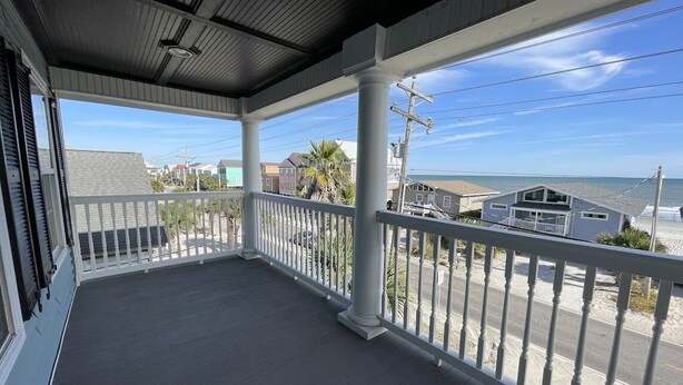A covered porch with a white railing, overlooking a beach with houses and a clear sky. - Nana's Nook - Second Row in Garden City Beach (Garden City)