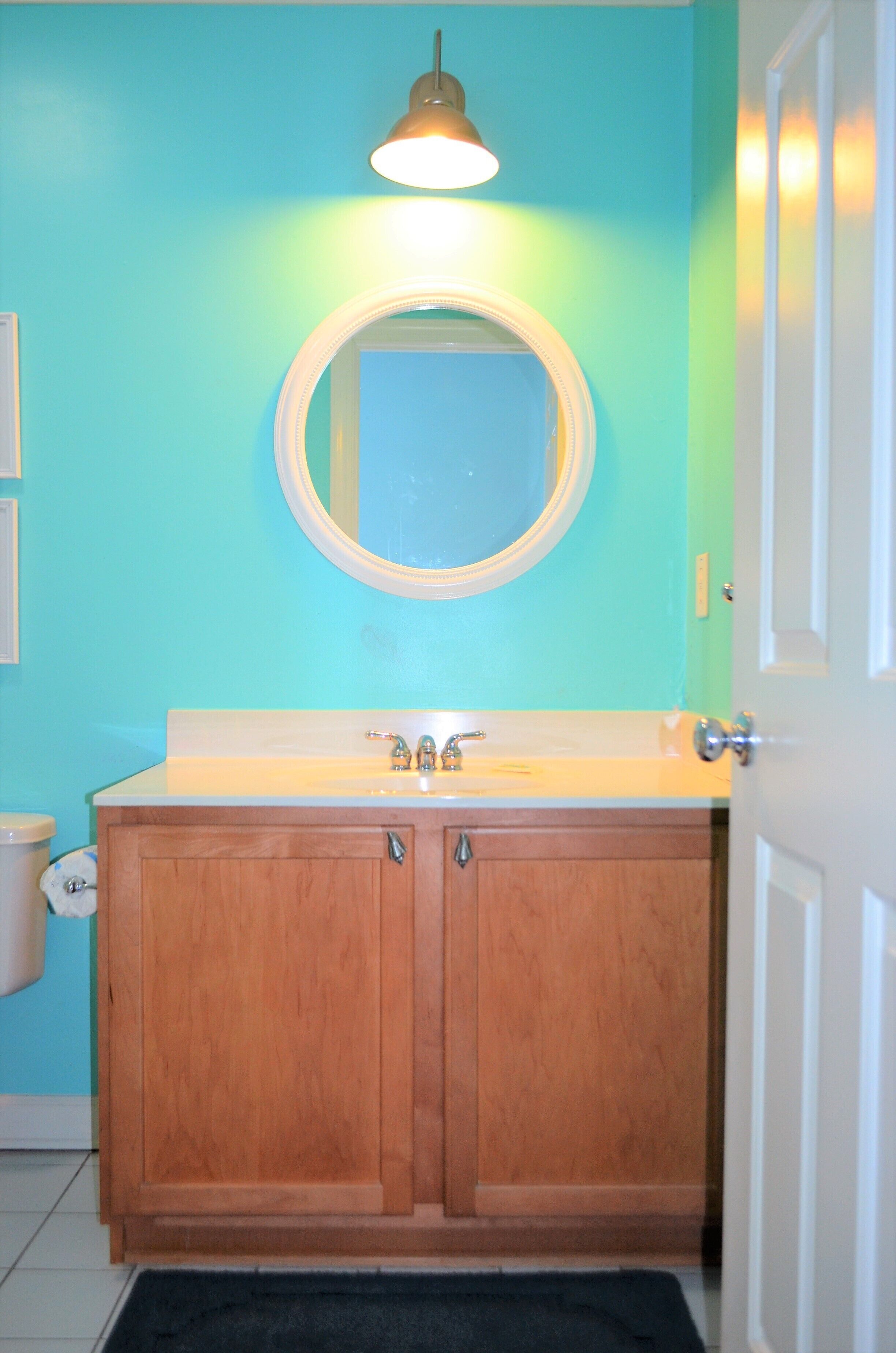 A bathroom with a wooden vanity, a round mirror, and a light fixture above the mirror.