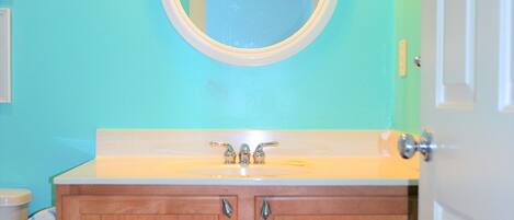 A bathroom with a wooden vanity, a round mirror, and a light fixture above the mirror.