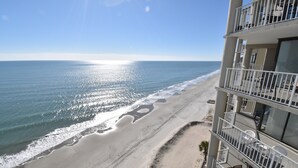 A beachfront hotel with multiple balconies, a sandy beach, and a clear view of the ocean. - One Ocean Place 1104 - Oceanfront Condominium in Garden City Beach (Garden City)