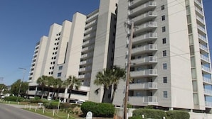 A multi-story residential building with balconies, a parking garage, and palm trees. - One Ocean Place 1104 - Oceanfront Condominium in Garden City Beach (Garden City)