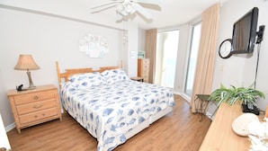 A bedroom with a bed, wooden dresser, bedside lamp, ceiling fan, and a view of the outdoors. - One Ocean Place 1104 - Oceanfront Condominium in Garden City Beach (Garden City)