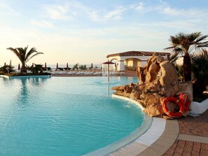 A swimming pool with a rock feature, lounge chairs, and umbrellas. - La Plage (Sorso)