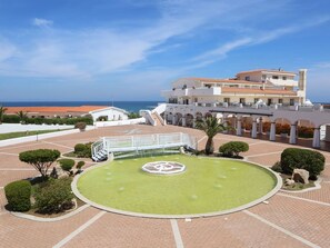 A hotel courtyard with a central fountain, a white building with balconies, and a view of the sea. - La Plage (Sorso)