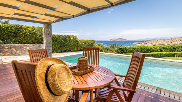 A wooden deck with a pool, chairs, and a table.