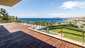 A wooden deck with a glass balustrade overlooking a coastal landscape.