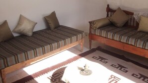 Een kamer met twee houten banken met gestreepte kussens, een kleine tafel met een decoratief object, en een kamerbreed tapijt op de vloer.