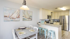 A modern kitchen with white cabinets, a stainless steel refrigerator, and a dining area with a table set for four. - Modern Ground Floor Condo w/ 2 Pools, Beach Access + Free Attraction Tickets! (Santa Rosa Beach)