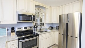 A kitchen with white cabinetry, a stainless steel refrigerator, a microwave, a stove, and a sink. - Modern Ground Floor Condo w/ 2 Pools, Beach Access + Free Attraction Tickets! (Santa Rosa Beach)