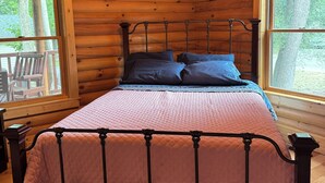 Ein Schlafzimmer einer Holzhütte mit einem Metallbettgestell, einem Deckenventilator und großen Fenstern.