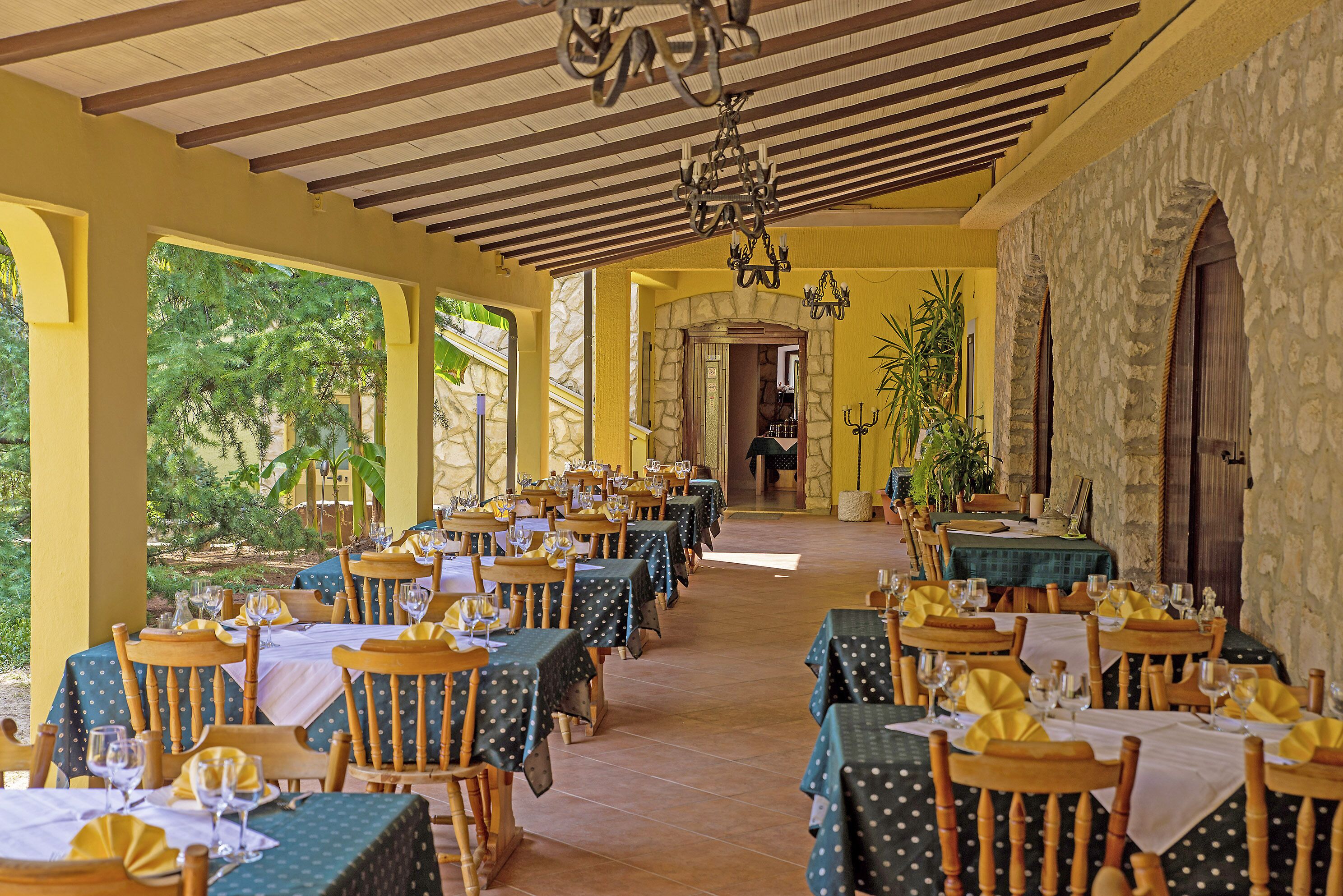 A restaurant with multiple tables set for dining, featuring a stone wall and wooden ceiling.