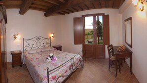 Quarto com cama, mesas de cabeceira, escrivaninha e janela com persianas.