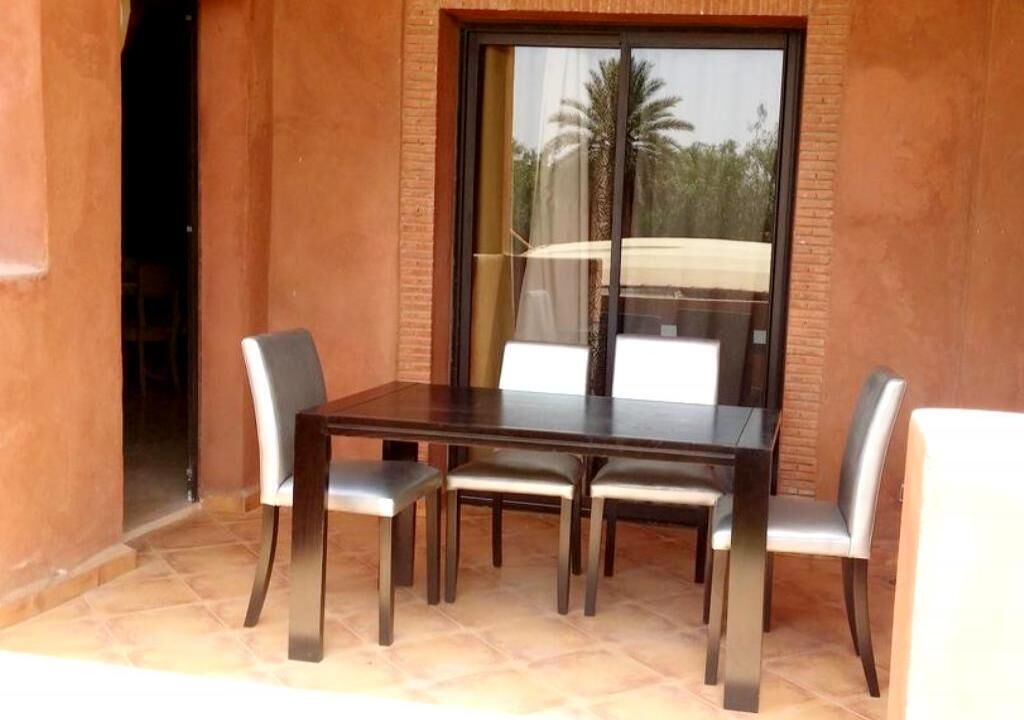 A dining area with a table and four chairs, a sliding glass door, and a view of palm trees.