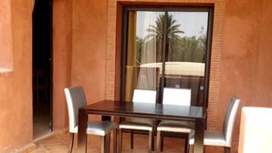 Een eetruimte met een tafel en vier stoelen, een schuifdeur en uitzicht op palmbomen.