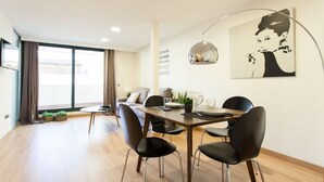 A modern dining area with a wooden table and black chairs, a coffee machine, and a large window with curtains. - Albareda 5 - One Bedroom Apartment, Sleeps 4 (Sevilla)