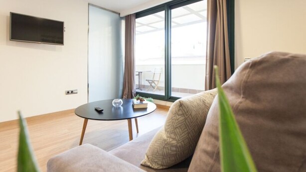 A modern living room with a sofa, a small round table, and a TV mounted on the wall. - Albareda 5 - One Bedroom Apartment, Sleeps 4 (Sevilla)