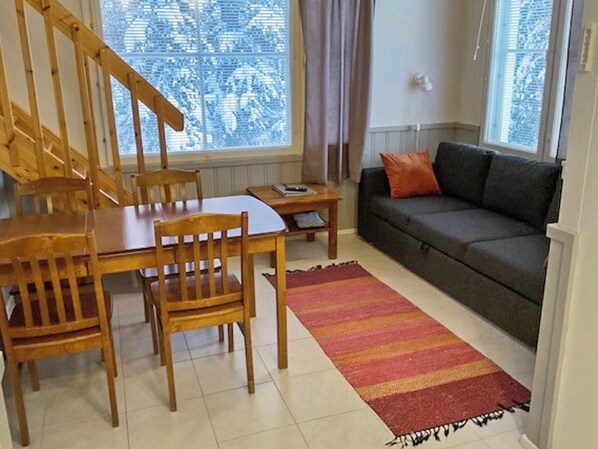 Un área de comedor con una mesa y sillas de madera, un sofá y una ventana con vistas a árboles.