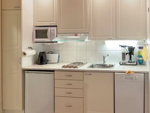 Una cocina moderna con armarios blancos, microondas, cafetera y lavavajillas.