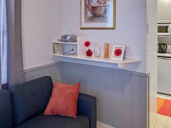 A modern living room with a grey sofa, a red cushion, and a white shelf with decorative items.