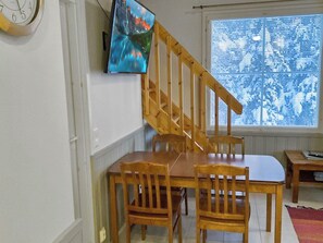 A dining area with a wooden table and chairs, a wall-mounted clock, and a window with blinds.