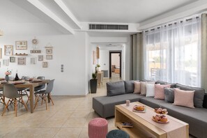 A modern living room with a grey sofa, wooden coffee table, and a dining area with a wooden table and chairs.