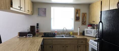 A kitchen with wooden cabinets, a black refrigerator, a microwave, and a window providing natural light.