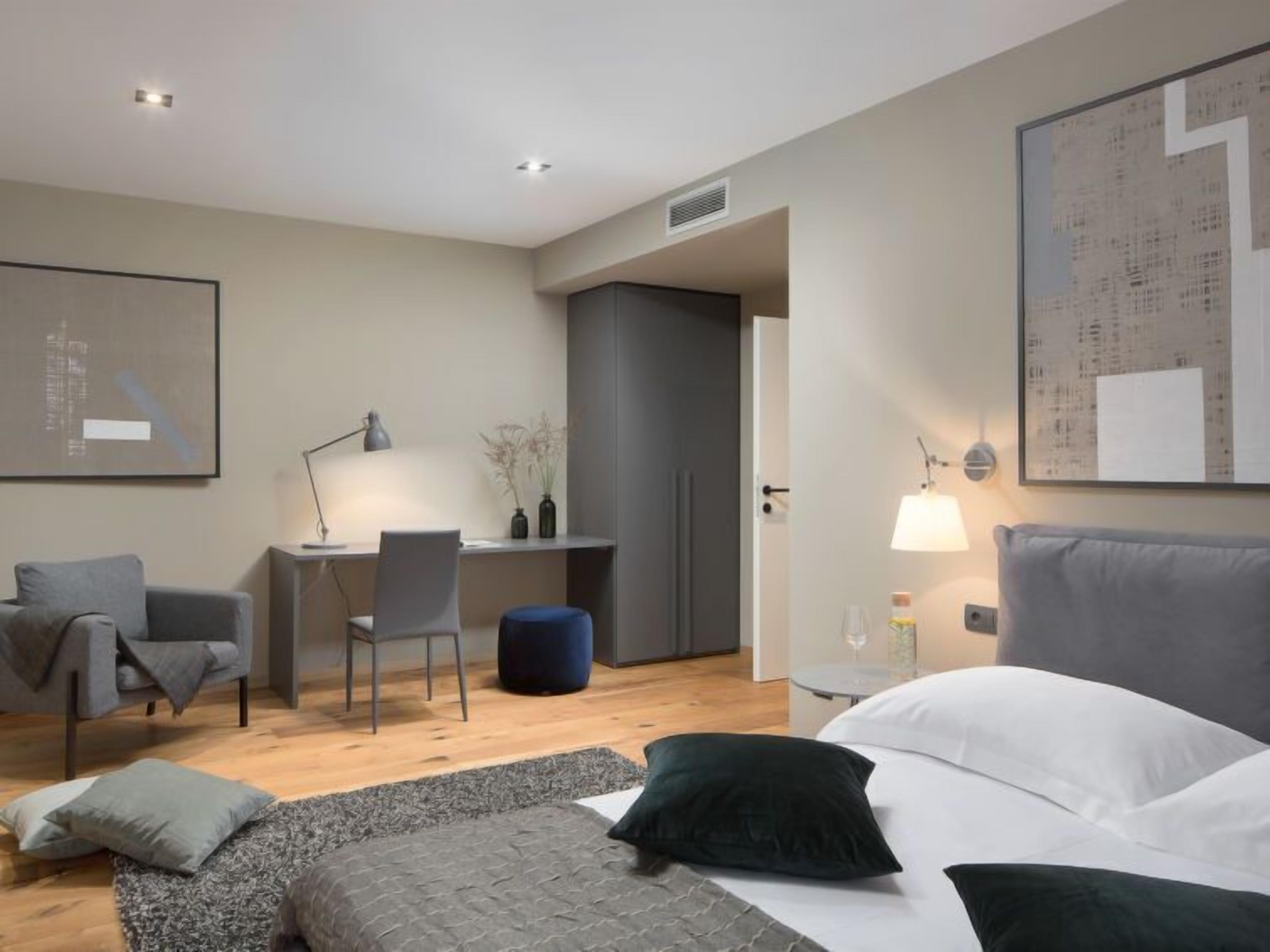 A modern hotel room with a bed, a desk, a chair, and a sofa.