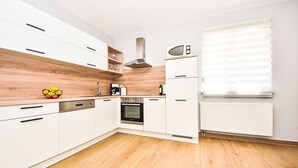 A modern kitchen with white cabinets, a wooden backsplash, a built-in oven, and a window with blinds. - Vacation home Anić by Interhome (Novigrad (Zadar))