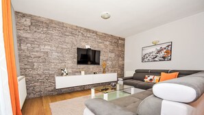 A modern living room with a stone wall, a flat-screen TV, a grey sofa, and a glass coffee table. - Vacation home Anić by Interhome (Novigrad (Zadar))