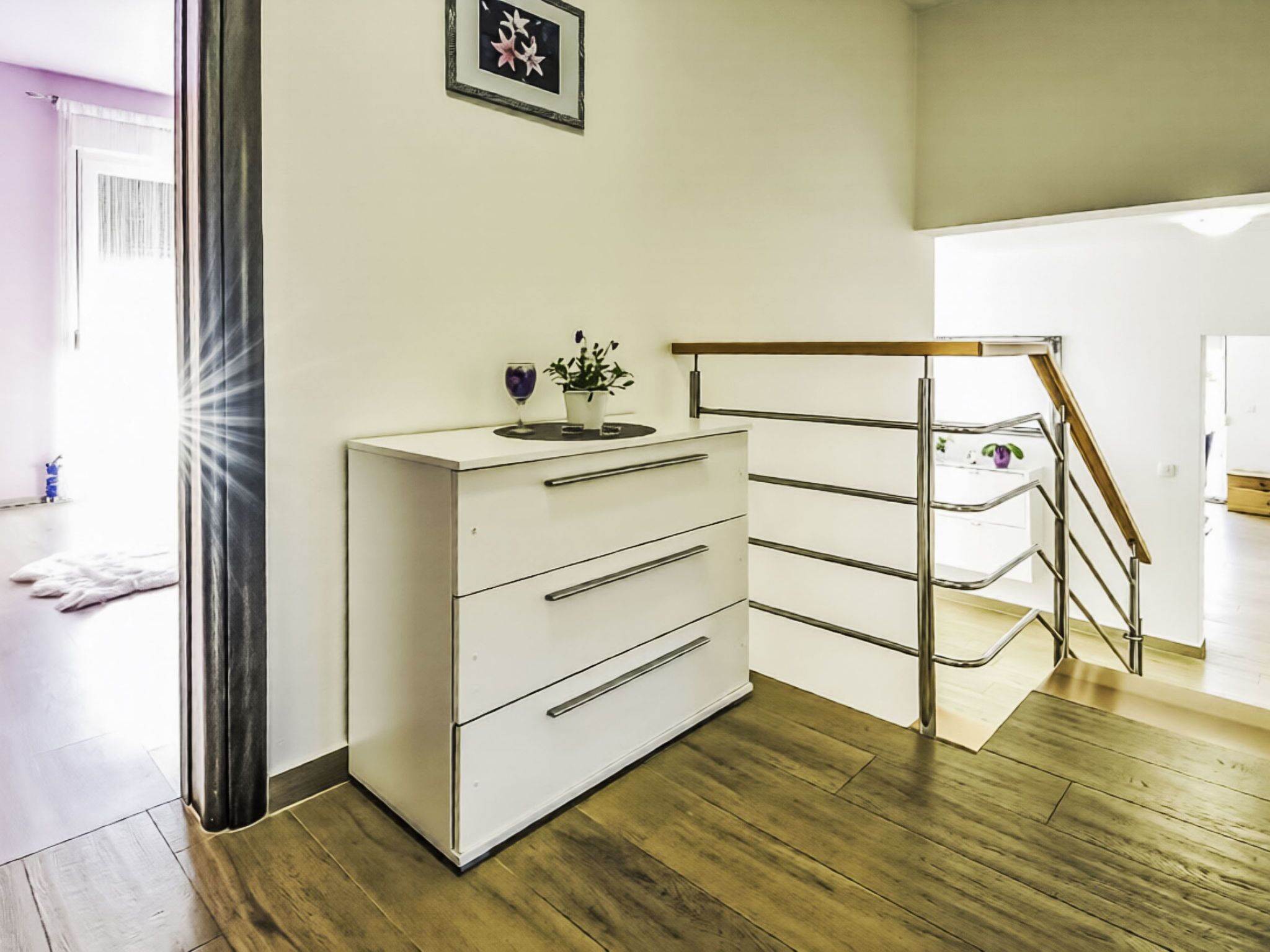 Ein modernes Zimmer mit weißem Schminktisch, Holzboden, einer Treppe und einem gerahmten Bild an der Wand.