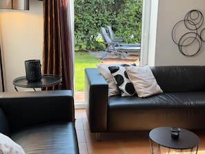 A modern living room with a leather sofa, a round coffee table, and a view of a garden through a glass door. - To complete (Niedersachsen)
