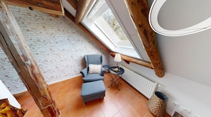 A loft bedroom with a sloped ceiling, a blue armchair, a small round table, and a radiator.