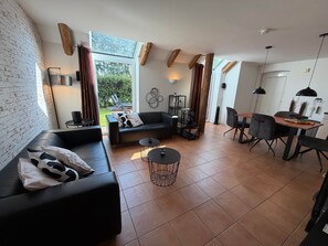 A modern living space with a black leather sofa, a round coffee table, and a dining area with a wooden table and chairs.