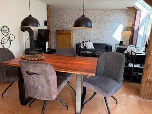 Uma sala de jantar com uma mesa de madeira, cadeiras estofadas cinzas e luminárias pendentes pretas.
