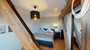 Una camera da letto con soffitto a loft, travi in legno a vista, un letto con cuscini decorati, un comodino con una lampada e una parete in mattoni.