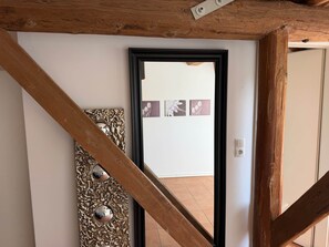 Uma escadaria com vigas de madeira, um espelho decorativo fixado na parede e uma porta que dá para outro quarto.