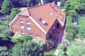 A two-story brick house with a sloped roof, multiple windows, and a garden with various plants and flowers.
