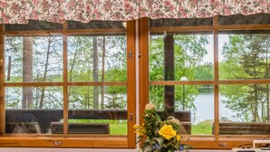 Een chalet met grote ramen met uitzicht op een meer, een houten tafel met een bloemenvaas, en een radio op de tafel.