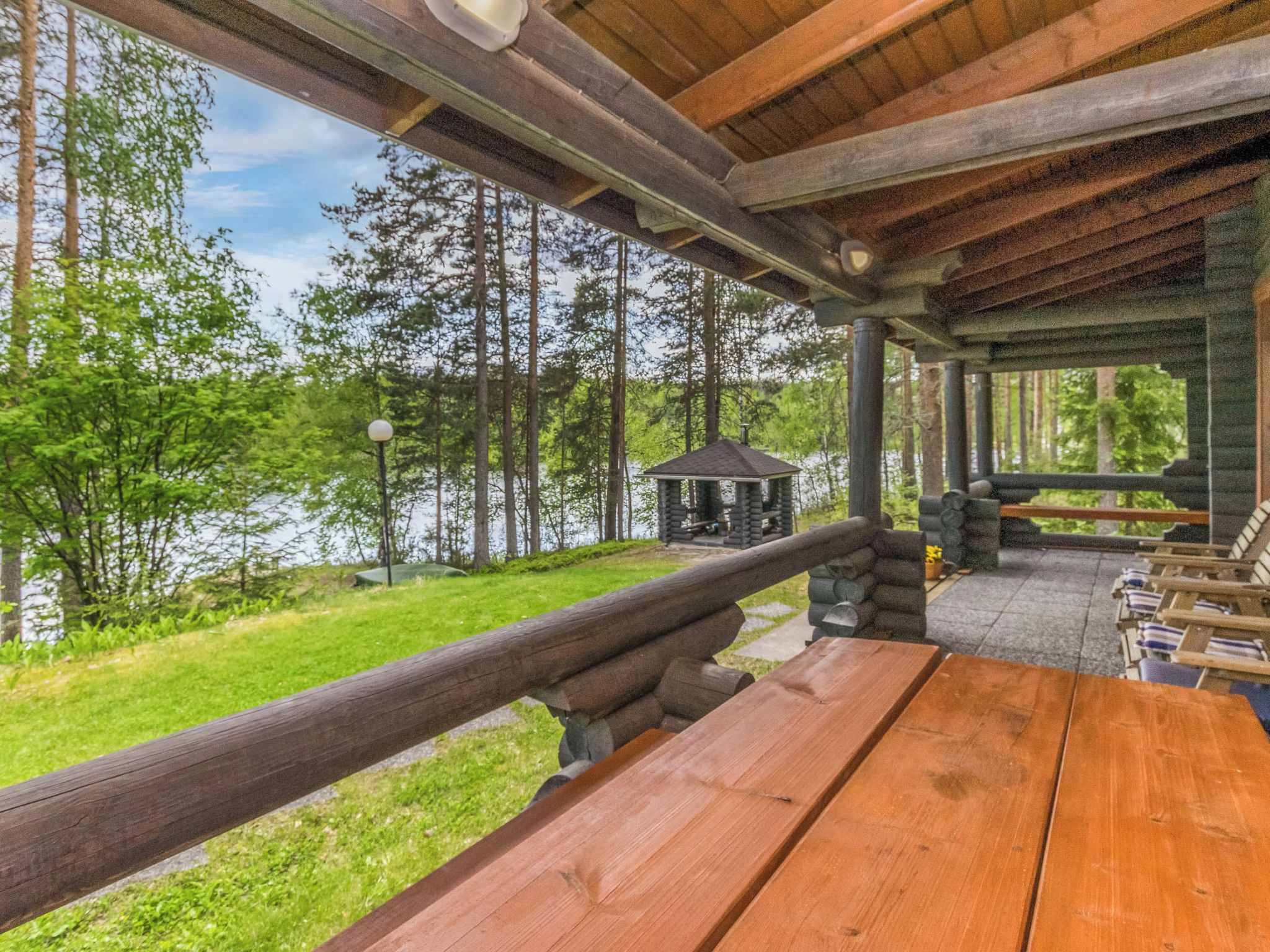 A wooden deck with a view of a lake and forest, a gazebo, and lounge chairs.