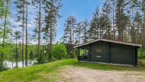 Een chalet met een veranda, omgeven door hoge bomen en een meer.