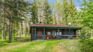 Een vakantiehuisje van hout met een veranda, omgeven door hoge bomen en een gazon.
