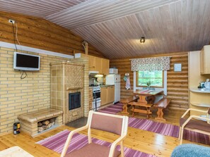 A cozy cabin interior with a fireplace, wooden walls, a kitchen area, and a dining table. - Lohi, cjoe237 a by Interhome (Heinävesi)