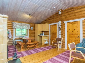 A cozy cabin interior with a wooden dining table, benches, a kitchen area, and a seating area with a chair and a sofa. - Lohi, cjoe237 a by Interhome (Heinävesi)